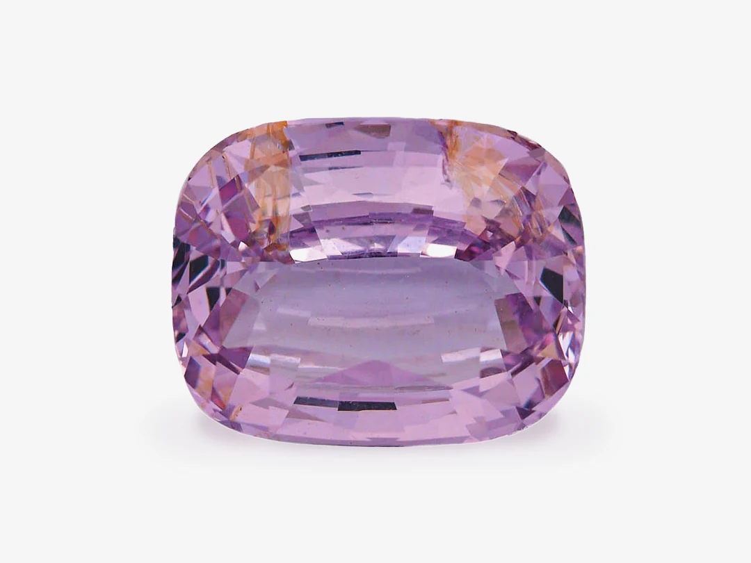 A loose purple spinel, 5.06 carats, cushion cut, seen face-up on a light grey background, with a large table, a paler centre and orange patches near the upper edge