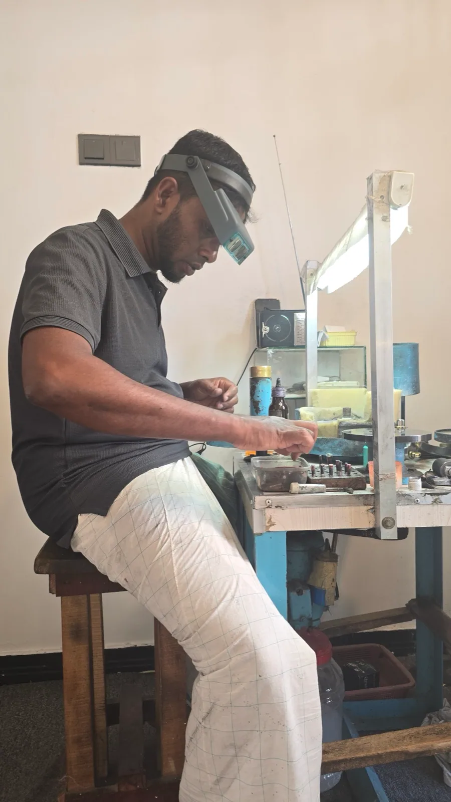A gem cutter wearing a loupe headband working at a faceting machine
