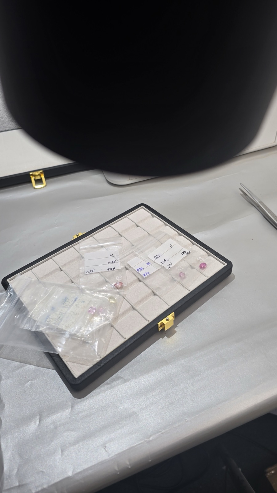 A gemstone parcel case with loose stones and tweezers on a sorting table