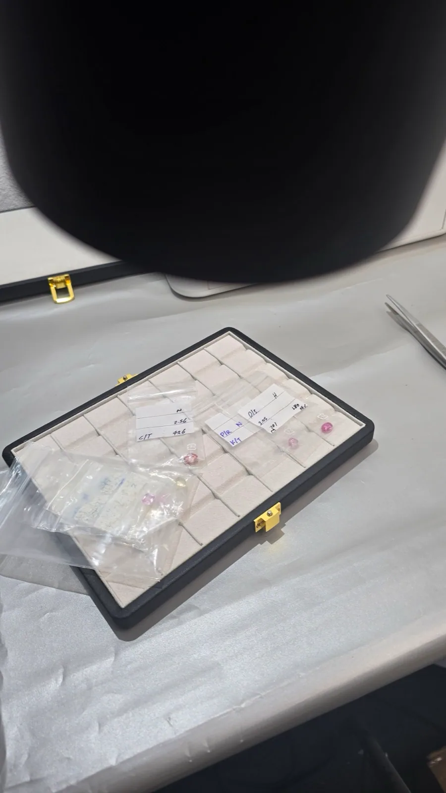A gemstone parcel case with loose stones and tweezers on a sorting table