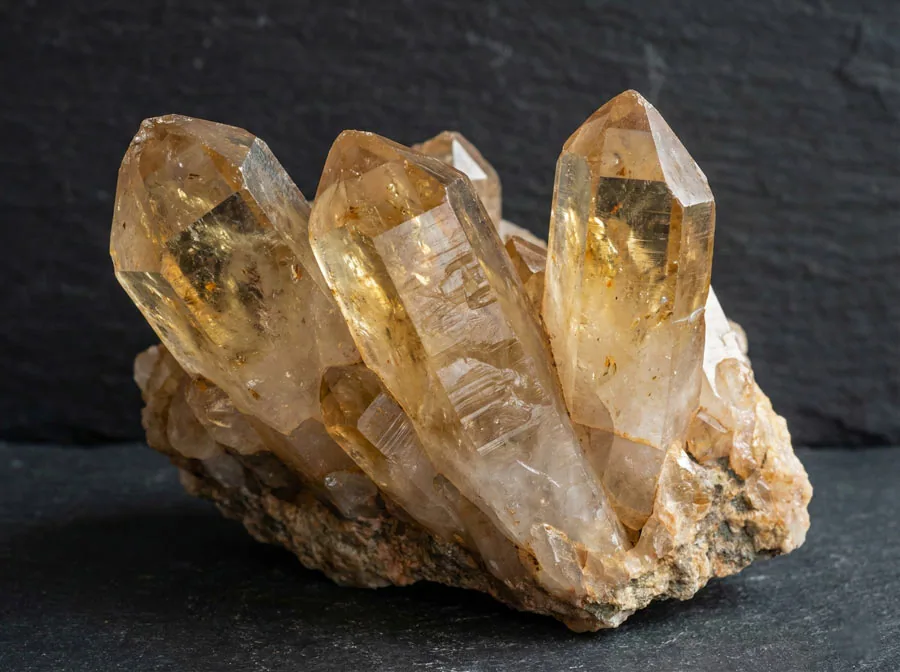 Cluster de cristaux de citrine naturelle sur matrice, montrant la formation hexagonale du quartz avec une coloration miel doré, photographié en lumière naturelle sur fond de pierre sombre
